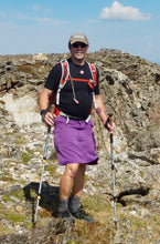 Man hiking in the mountains with trekking poles and wearing a hiking skirt for men.